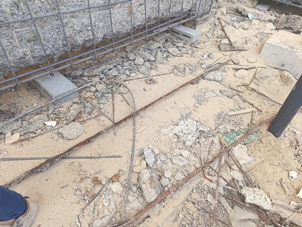 Reinforced concrete beam with cover broken out, exposing corroded reinforcement during repair